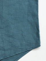 A close-up of the Blue de Gênes BGenric Hope L/S Shirt in Green Harvest showcases its textured weave and sewn edges, reminiscent of breathable linen, with a slightly folded bottom corner against a white background.