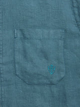 A close-up of the BGenric Hope L/S Shirt - Green Harvest by Blue de Gênes shows its teal linen pocket with visible stitching and a blue embroidered shield emblem—ideal as a breathable summer shirt.