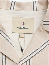 Close-up of the BGcody Fling Shirt in Pale Khaki by Blue de Gênes, featuring a dark striped collar. The inside label displays the Blue de Gênes name with a red and white shield logo, plus an L size tag hanging on a string.