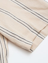 Close-up of the BGcody Fling Shirt - Pale Khaki by Blue de Gênes, featuring thin black vertical stripes on textured, soft fabric. The relaxed, oversized fit and folded edge evoke effortless resort style against a white background.