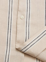Close-up of the BGcody Fling Shirt - Pale Khaki by Blue de Gênes, featuring an oversized beige linen design with black and white vertical stripes, a visible button, and a folded bottom right corner.