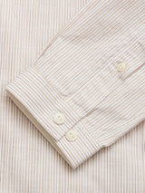 A close-up of the Blue de Gênes BGbasso Meco Shirt - Beige Stripe sleeve with white buttons, laid flat on matching 100% cotton fabric. The beige and white stripes add a classic touch. Made in Portugal.