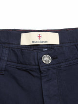 Close-up of the waistband on BGmenzino Vecchio Shorts - Dark Navy by Blue de Gênes, featuring a metallic button, belt loop, and a Blue de Gênes label beneath a small shield emblem.