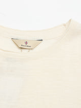 A close-up of the collar and neckline of the BGmonty Knit - Chalk, a cream-hued Blue de Gênes t-shirt in a soft cotton linen blend, featuring a fabric tag with the brand name and a small shield logo.
