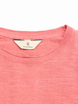 A close-up of the BGmonty Knit - Coral by Blue de Gênes, highlighting the pink crew neck, beige label with Blue de Gênes and crest logo, and the heathered cotton-linen blend fabric for comfort.