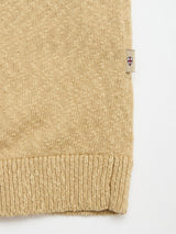 Close-up of the BGyale Slubby Crewneck Knit in Pale Khaki by Blue de Gênes, showing the textured cotton knit, ribbed hem, and a small fabric tag with a red cross emblem sewn into the side seam.