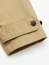 Close-up of the BGjacques Coat by Blue de Gênes in pale khaki heavy cotton, showing a relaxed sleeve with matching strap and black button detail near the cuff, set against a white background.