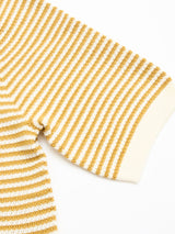 A close-up of the Blue de Gênes BGbob Knit Polo - Sunflower shows textured cotton knit with horizontal mustard yellow and white stripes, evoking a nautical look, and finished with a solid white ribbed cuff on the short sleeve.