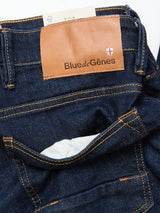 Close-up of the Vinci Pala Dark V2 Jeans by Blue de Gênes in dark blue denim, regular fit with orange stitching, a brown leather Blue de Gênes patch and shield emblem on the waistband, made from comfort stretch fabric for daily wear.