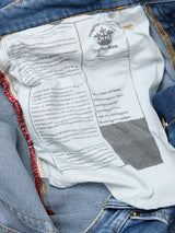 Close-up of the inside of Blue de Gênes Vinci Pala Used V2 Jeans in denim blue, showing a white label with black print and red stitching along the seam; text reveals regular fit, made in Italy, with some faded or obscured details.