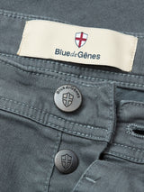 Close-up of the Paulo Pavia 1 V2 Chino in charcoal by Blue de Gênes, showcasing metal buttons and a fabric label with the brands name and shield logo, crafted from premium cotton stretch fabric.