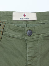 Close-up of Paulo Pavia 1 V2 Chino - Army by Blue de Gênes in green cotton stretch, featuring a metal button, signature label above the waistband, and a shield logo with a red cross plus orange stitching near the pocket.