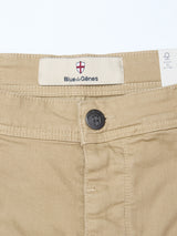 Close-up of the waistband of Blue de GĂȘnes Paulo Pavia 1 V2 Chino in khaki, showing a metal button with engraved shield, a Blue de GĂȘnes label with red and white shield logo, and a white care tag inside.