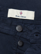 Close-up of Midnight Blue Paulo Pavia 1 V2 Chino by Blue de Gênes in cotton stretch, with a label displaying a red and white shield logo, two metal buttons featuring the shield, and subtle vintage military-inspired design details.
