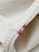 Close-up of the BGpaulo Pavia 1 V2 Chino in ecru by Blue de Gênes, featuring cream-colored cotton stretch denim with visible stitching and two small red embroidered accents, inspired by vintage military pants.