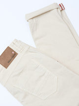 A pair of BGpaulo Pavia 1 V2 Chino pants in ecru by Blue de Gênes, neatly folded to show the brown leather “Blue Genes” patch and back pocket, crafted from cotton stretch fabric and displayed on a white background.