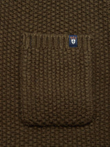 The close-up reveals the coarse pearl knit fabric and small pocket of the Aimone Knit Cardigan - Army by Blue de GĂȘnes. A blue tag on the pocket features a crown and cross symbol, exuding classic allure.