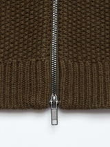 Close-up of a metal zipper on the textured knit fabric of the Aimone Knit Cardigan - Army by Blue de GĂȘnes, showcasing its vertical placement against the woven pattern and ribbed hem, crafted from luxurious lambswool.