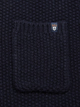 Close-up of textured dark navy lambswool fabric from the Blue de Gênes Aimone Knit Cardigan. A small center pocket has a label with an orange design and cross symbol, evoking classic knit cardigan style.