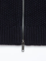 Close-up of a metal zipper on the Aimone Knit Cardigan in Dark Navy by Blue de Gênes, half-open to reveal the bumpy texture of coarse pearl knit, with shiny teeth contrasting beautifully against the rich pattern of thick-knit lambswool.