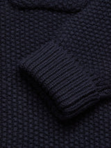 Close-up of a Dark Navy Aimone Knit Cardigan by Blue de Gênes, highlighting its sleeve and body. The lambswool fabric features a coarse pearl knit pattern with ribbed cuffs, offering a soft and warm texture.
