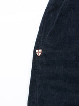 Close-up of the Albi Cargo Pant in Dark Navy by Blue de Gênes, showcasing dark blue corduroy fabric with a vertical ridge design that enhances comfort. A red and white cross emblem patch is on the right, complementing its loose fit and reminiscent of classic cargo pants.
