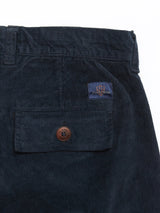 A close-up of Blue de Gênes Albi Cargo Pant in dark navy corduroy reveals a pocket with a brown button and an embroidered emblem tag. The ribbed texture and signature cross-cord comfort are clearly visible, reminiscent of classic cargo pants.