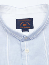 A close-up of the Basso Hackney Shirt by Blue de Gênes reveals a light blue and white striped cotton design with a mandarin collar. White buttons add subtle charm, while fine logo embroidery showcases refined craftsmanship. The label reads Pirrotta Herring, Liguria di Genova.