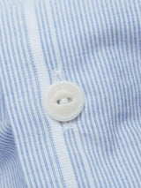 Close-up of a Basso Hackney Shirt - Blue Stripe by Blue de Gênes, showcasing quality cotton fabric with blue and white vertical stripes and a white button fastened through a buttonhole, hinting at possible logo embroidery beyond the frame.