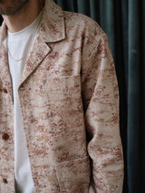 A person wearing the Blue de Gênes BGkendrick Print Jacket - Multi Pattern over a white t-shirt and a thin chain necklace stands in front of dark green curtains. The photo is cropped to show only the upper torso.