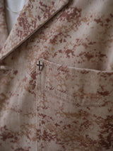 A close-up of the Blue de Gênes BGkendrick Print Jacket - Multi Pattern, a cotton twill worker jacket with beige and brown camo print and a small pin with a red cross on the chest pocket.