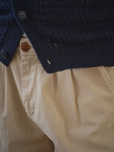 Close-up of a person wearing Blue de Gênes BGcopple Rodas Shorts in Pale Khaki with pleat front and brown button, paired with a navy blue textured sweater or cardigan.