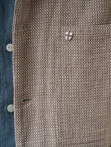 A close-up of the BGjazzy Ola Jacket - Dark Sand by Blue de Gênes, a brown cotton-linen blend summer jacket with white buttons and a pocket adorned by a small shield-shaped pin with a cross design.