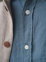 Close-up of the Blue de Gênes BGenric Hope L/S Shirt in Green Harvest, showing its breathable fabric and button details, partly covered by a beige textured jacket with a brown button. Focus is on fabric texture and buttons.