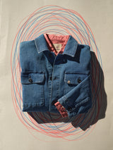 A neatly folded Blue de Gênes BGenric Hope L/S Shirt - Coral sits on a beige surface, layered under a blue denim jacket, with overlapping blue and red oval scribbles drawn around it.