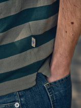 A close-up of a person wearing the BGwally Stripe Polo - Shadow Green by Blue de Gênes and blue jeans. Their right hand is in their pocket, showing part of their bare arm.