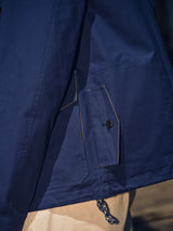 Close-up of the BGcanopy Jacket - Navy Peony by Blue de Gênes: a heavy cotton utility jacket featuring a buttoned pocket, visible stitching, and a blue-white patterned drawstring at the hem, worn over light-colored pants for classic workwear style.
