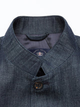 A close-up of the Casella Wasabi Blazer - Denim Blue from Blue de Gênes highlights its dark denim texture and stand-up collar with buffalo horn buttons, including a fastened top button and a visible dark tag inside the collar, showcasing the allure of dry denim craftsmanship.