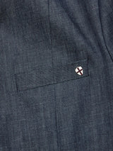 Close-up of dark dry denim fabric with a small rectangular pocket, topped by a Buffalo horn button with a red and white cross emblem, echoing the timeless charm of Blue de Gênes Casella Wasabi Blazer in Denim Blue.