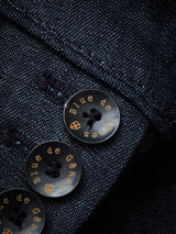 Close-up of a Denim Blue fabric from the Casella Wasabi Blazer by Blue de Gênes, featuring three Buffalo horn buttons with Blue de Gênes inscribed in gold. The vibrant texture resembles the fine weave of an Officers Blazer.
