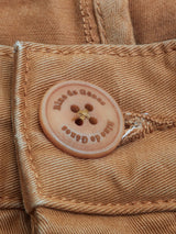 Close-up of a Biscotto Franco Genes Chino with a button fastened through a buttonhole. The button is inscribed with Blue de Gênes. The Saia twill fabric features visible stitching and a slightly worn texture, enhancing its lived-in charm.