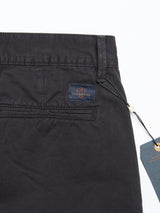 Close-up of the Franco Genes Chino in Charcoal by Blue de Gênes. These feature a back pocket with a stitched brand patch and have a tag attached to the waistband with a black string. Made from garment-dyed fabric, they offer a smooth texture and visible belt loops.