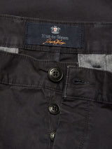 Close-up of Franco Genes Chino - Charcoal by Blue de Gênes, featuring a button fly with black buttons and an interior label with text and a small emblem. Made from Saia twill fabric, it has a slightly textured look and is garment-dyed for deep color.
