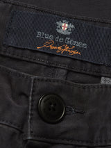 Close-up of the Franco Genes Chino - Charcoal from Blue de Gênes, featuring a brand logo and orange signature. A black button with brand text complements the smooth fabric texture and detailed Saia twill stitching.