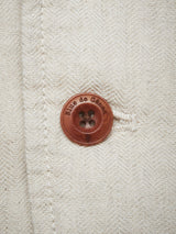 Close-up of a light beige cotton linen fabric with a stitched seam and a brown button engraved with Blue de Gênes, enhancing the charm of this herringbone-patterned piece from the Gabbiano Winnot Blazer - Natural.