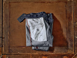 A pair of Giacomo 77 Dark Used Jeans - Mid Blue Denim by Blue de Gênes, featuring a relaxed loose fit and crafted from rigid denim, is folded with visible button details and a black tag on a rustic wooden surface. The inner lining displays printed text and a signature design.