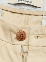Close-up of BGcopple Rodas Shorts in pale khaki by Blue de Gênes, featuring a cotton hemp blend, brown branded button, metal zipper partially unzipped, and a cream Blue de Gênes label on the waistband.