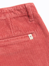 Close-up of Blue de Gênes BGfloyd Cord Shorts in Coral, featuring an elastic waistband, a back pocket, and a small white tag with red and blue shield emblem sewn on the pocket seam.