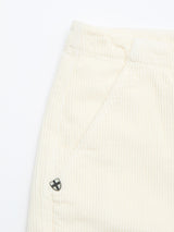 Close-up of BGfloyd Cord Shorts - Chalk by Blue de Gênes: cream-colored cotton corduroy shorts with a front pocket, loose fit, and a small metallic shield emblem with a black and white cross near the pocket seam.