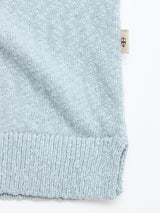 Close-up of the BGjohn Slubby Polo in Blue Fog by Blue de Gênes, showing its light blue knit, ribbed hem, and a small beige tag with a red and blue shield emblem on the side.